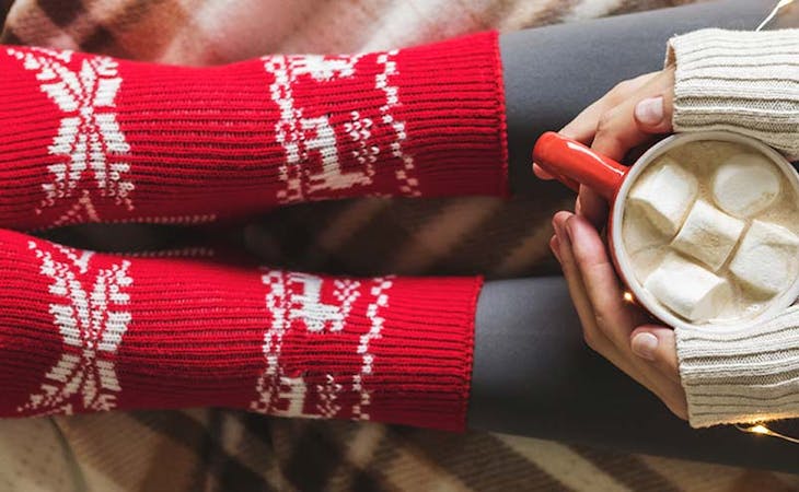 image of woman's feet in red socks holding hot chocolate in cozy winter bedroom