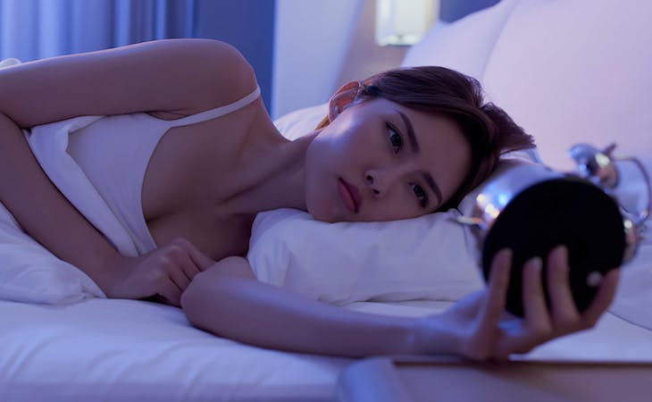 woman staring at alarm clock in bed having trouble going to sleep