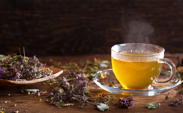 cup of herbal tea next to spoon with tea leaves on it