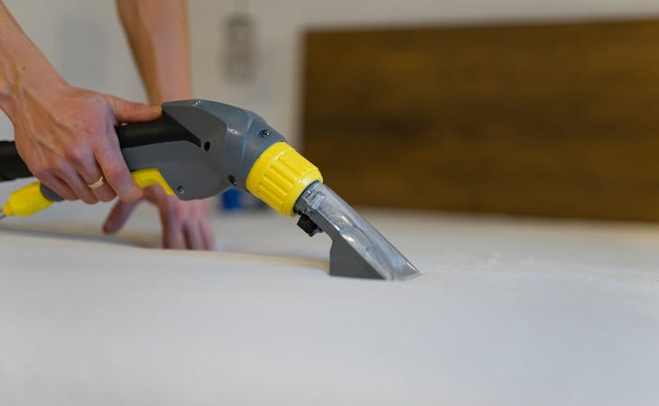 person cleaning a mattress with a vacuum cleaner