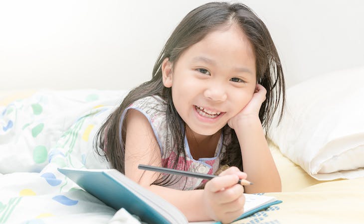 child writing in journal in bed