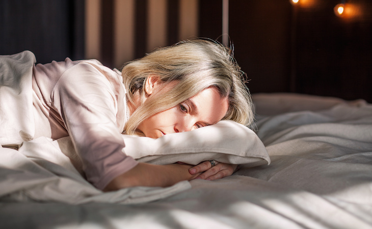 unhappy woman lying down on pillow and bed