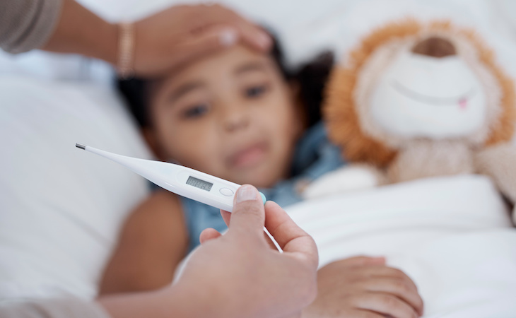 sick child lying in bed with parent taking temperature