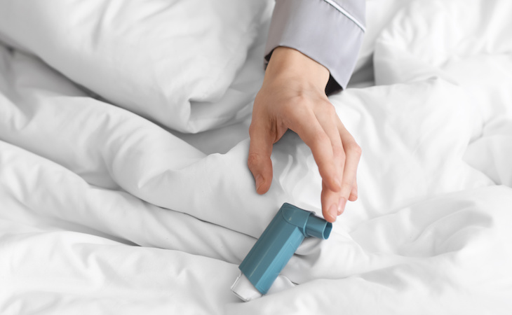person reaching for asthma inhaler in bed