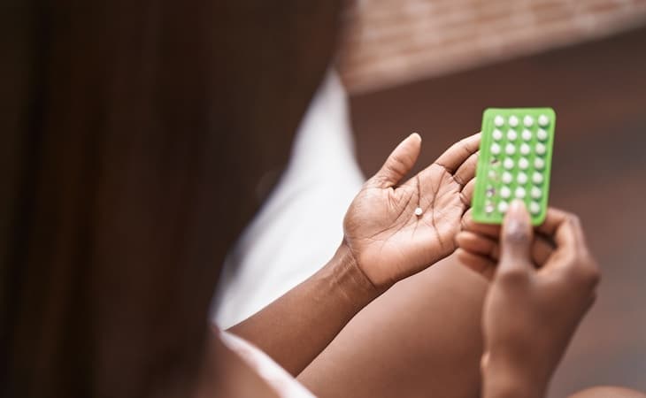 person holding birth control pills sitting on bed