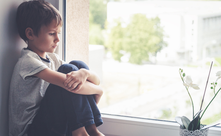 sad child sitting on window sill