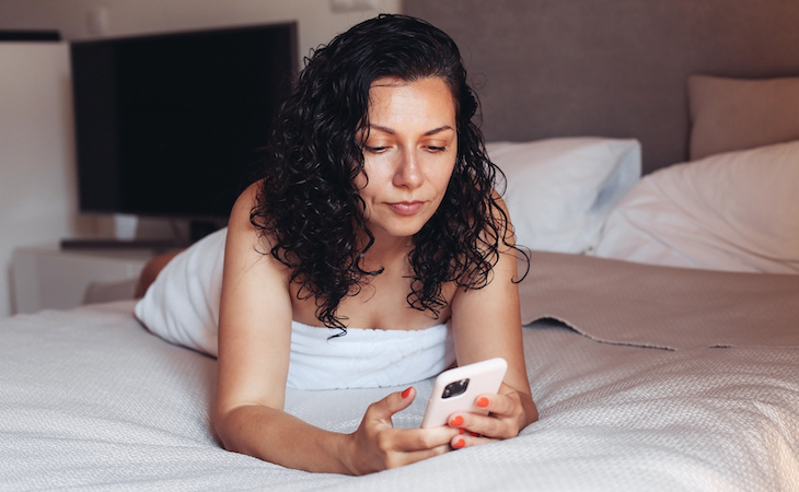 person lying on bed with wet hair looking at phone