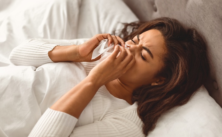 person sneezing and blowing nose in bed