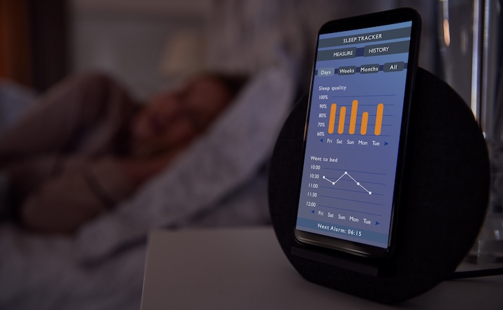person sleeping in bed with sleep data app running on mobile phone on bedside