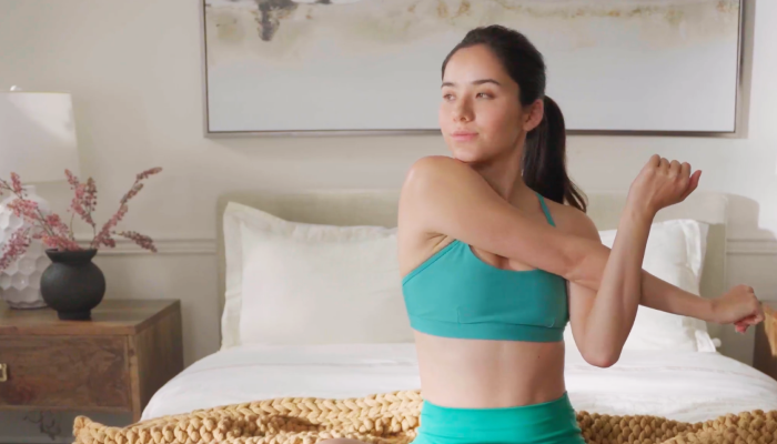 woman stretching arm while sitting on bed