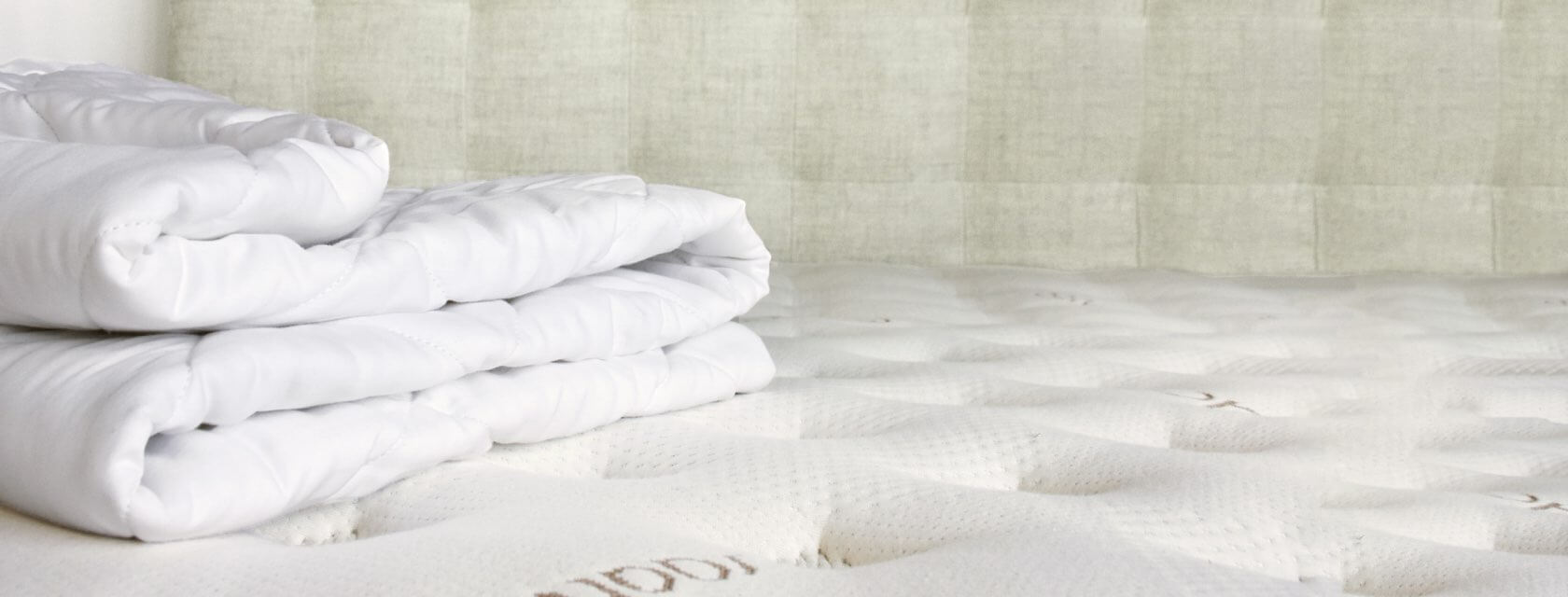 A Saatva mattress pad folded up on a Saatva mattress.