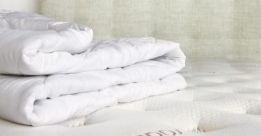 A Saatva mattress pad folded up on a Saatva mattress.